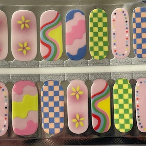 Puede incluir: Lámina de pegatinas para uñas con varios diseños. Algunas tienen fondos rosas con flores, mientras que otras presentan patrones coloridos como cuadros, líneas onduladas y rayas arcoíris. Las pegatinas tienen varias formas.