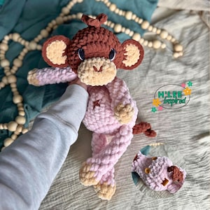 Könnte beinhalten: Handgemachte Häkelpuppe eines Affen in Braun-, Beige- und Rosatönen. Der Affe hat große Ohren, ein lächelndes Gesicht und ein Sternendetail auf der Brust. Die Puppe ist weich und plüschig, mit einem langen Schwanz und Gliedmaßen.