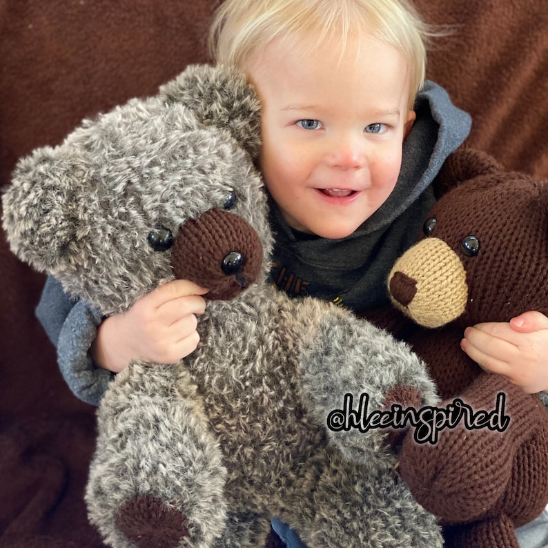 Op de afbeelding: Een jong kind houdt twee pluche teddyberen vast. De ene beer is bruin en de andere is grijs met bruine accenten. Het kind draagt een grijs hoodie. De tekst "@hleeinspired" is zichtbaar in de afbeelding.