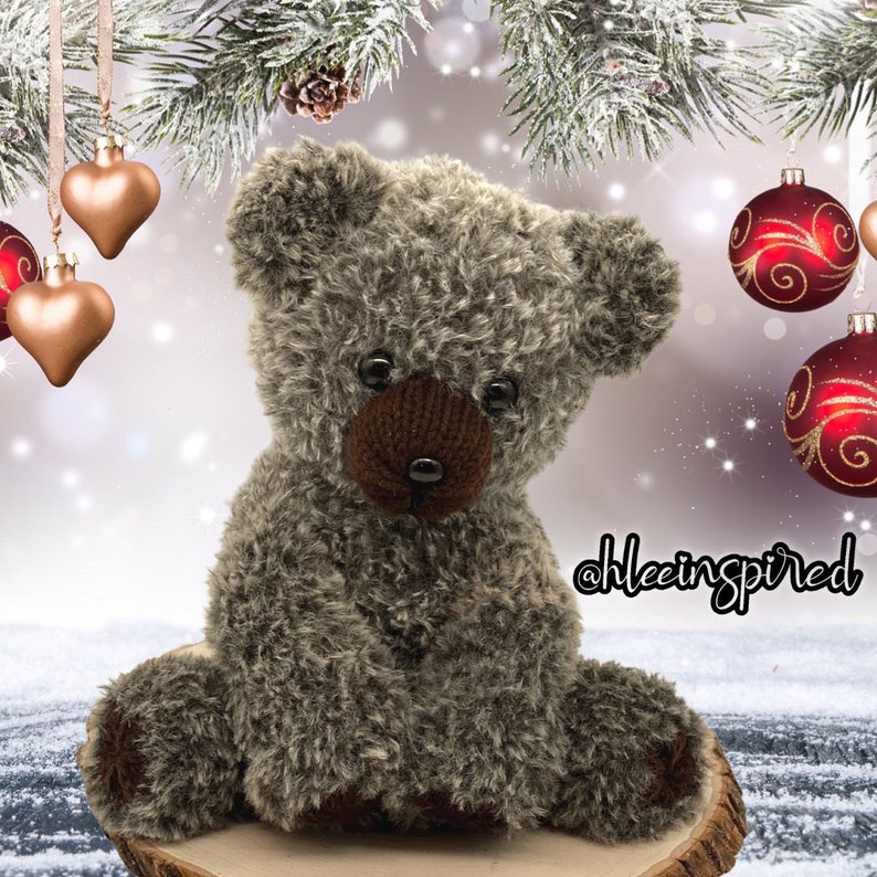 Op de afbeelding: Een pluche bruine teddybeer met een donzige textuur zit op een houten oppervlak. De beer heeft zwarte ogen en een bruine neus. De beer is omringd door kerstversiering, waaronder rode en gouden ornamenten.