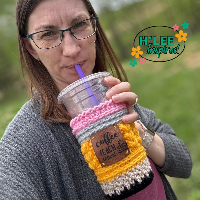 May include: A crocheted coffee cup cozy in yellow, pink, gray, and black with a brown leather patch that says "coffee teach repeat" and a small pencil icon.