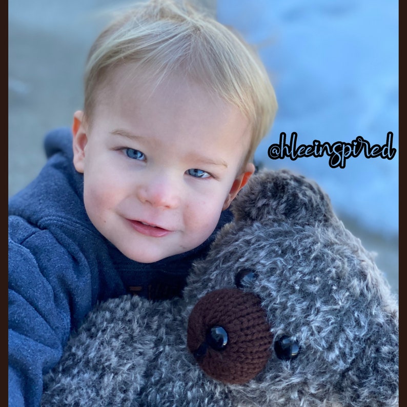 Op de afbeelding: Een jong kind met blond haar houdt een grijze en bruine pluche teddybeer vast. Het kind draagt een blauwe hoodie. De tekst "@hleeinspired" is zichtbaar op de achtergrond.