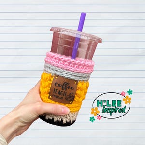 May include: A yellow, pink, gray, and black crocheted pencil-shaped cup cozy with a brown leather patch that says "coffee teach repeat" and a small image of a book and pencil.