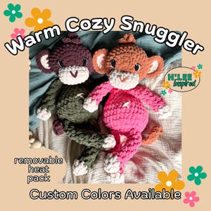 May include: Two handmade crochet monkey plush toys. One is dark green, the other is pink. Both have white faces, ears, and hands. The text "Warm Cozy Snuggler" and "Custom Colors Available" are visible.