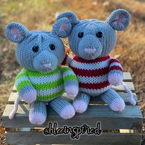 May include: Two knitted gray mice wearing striped sweaters. One mouse is wearing a green and white striped sweater, and the other is wearing a red and white striped sweater. The mice are sitting on a wooden crate.