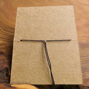 May include: A close-up of a black cord tied to a brown card with a silver bead in the center.