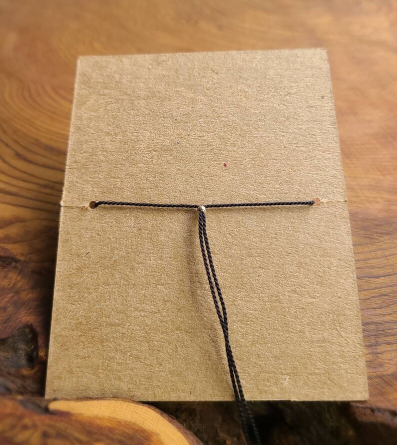 May include: A close-up of a black cord tied to a brown card with a silver bead in the center.