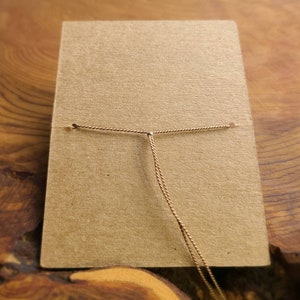 May include: A brown card with a gold cord tied through two holes at the top. The cord is knotted in the center.