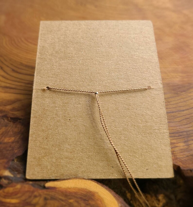 May include: A brown card with a gold cord tied through two holes at the top. The cord is knotted in the center.