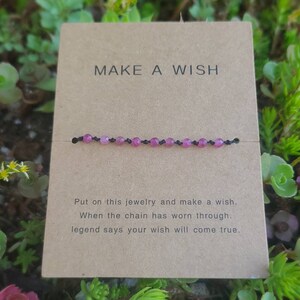 May include: A brown card with the text "MAKE A WISH" printed on it. A pink beaded bracelet is displayed on the card. The text below the bracelet reads "Put on this jewelry and make a wish. When the chain has worn through, legend says your wish will come true."