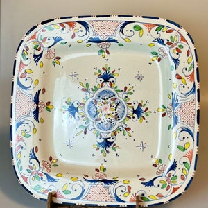 May include: Square ceramic serving platter with a cream base and a detailed floral design. The border is decorated with blue, red, yellow, and green floral patterns. The centre features a symmetrical floral motif in blue and white.
