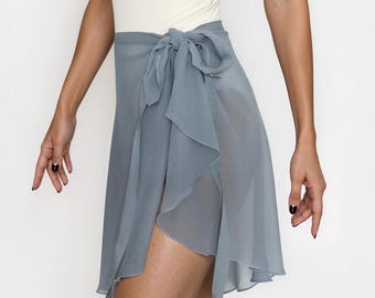 May include: A dusty blue wrap skirt made of a sheer, lightweight fabric. The skirt features a tie closure at the waist with a side knot, creating a layered, ruffled effect that drapes down the front with a high-low hemline and a side slit.