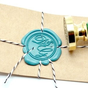 May include: A teal wax seal with a monogram on a kraft paper card tied with black and white twine. A gold and green wax stamp is positioned next to the seal. The card is labeled "Back to Zero".