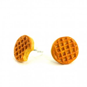 May include: A pair of waffle-shaped earrings, one with a bite taken out of it. The earrings are a light brown color and have a glossy finish.