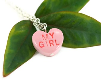 Op de afbeelding: Een ketting met een roze hartvormige hanger en een zilveren ketting. De hanger heeft de tekst "MY GIRL" in rood.