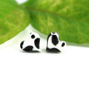 Puede incluir: Un par de pendientes en forma de corazón blanco y negro. Los corazones tienen un patrón de manchas blancas y negras.