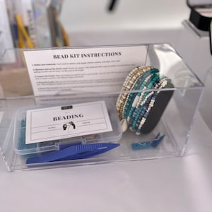 May include: A clear plastic container with a bead kit inside. The kit includes a variety of colorful beads, string, and tools for making jewelry. The container also includes a card with the instructions for the kit. The card says "Bead Kit Instructions".