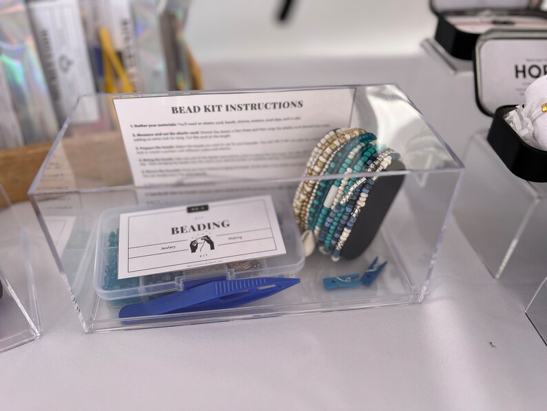 May include: A clear plastic container with a bead kit inside. The kit includes a variety of colorful beads, string, and tools for making jewelry. The container also includes a card with the instructions for the kit. The card says "Bead Kit Instructions".