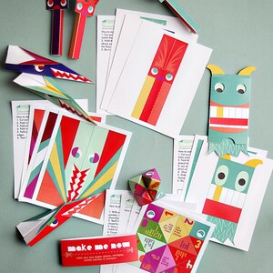 May include: A collection of colorful paper craft kits, including paper airplanes, monsters, and a geometric shape. The kits feature red, green, and yellow accents, with instructions and the text "make me now".