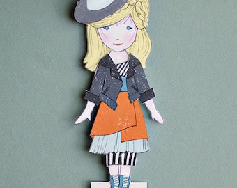 May include: A paper doll illustration of a girl named Willow, wearing a witch hat, black jacket, orange skirt, and striped dress. The doll has blonde hair and blue eyes. The word "willow" is printed on a white rectangle.