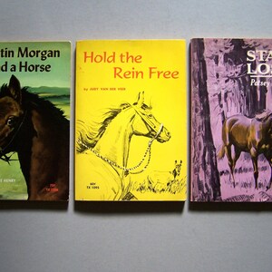 May include: Three vintage horse-themed books. The covers feature illustrations of horses and titles like "Justin Morgan Had a Horse," "Hold the Rein Free," and "Star Lost." The books are in various colors, including green, yellow, and purple.