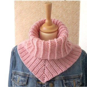 Könnte beinhalten: Ein rosa gestrickter Schal mit einem dreieckigen Kragen. Der Schal wird auf einer Jeansjacke präsentiert.