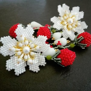 May include: White and red beaded flower earrings with a pearl center. The flowers are made of white beads and the stems are made of green and red beads.