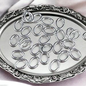 May include: A silver tray filled with a large quantity of oval-shaped jump rings. The jump rings are all the same size and are arranged in a random pattern.
