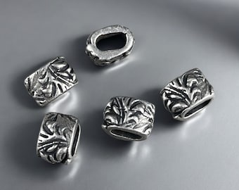 May include: Five silver-toned metal beads with a rectangular shape and a textured, raised leaf-like pattern on the surface. Each bead features a central horizontal opening, showcasing an oxidized finish that highlights the intricate details.
