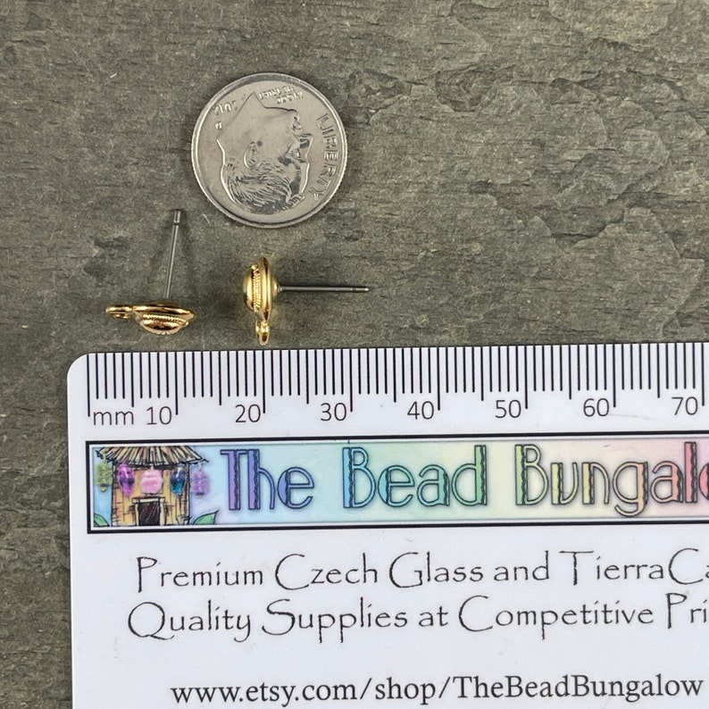 May include: Two gold-colored stud earrings with a spiral design, next to a U.S. dime and a ruler. The earrings are on a gray surface. The text "The Bead Bungalow" is visible.