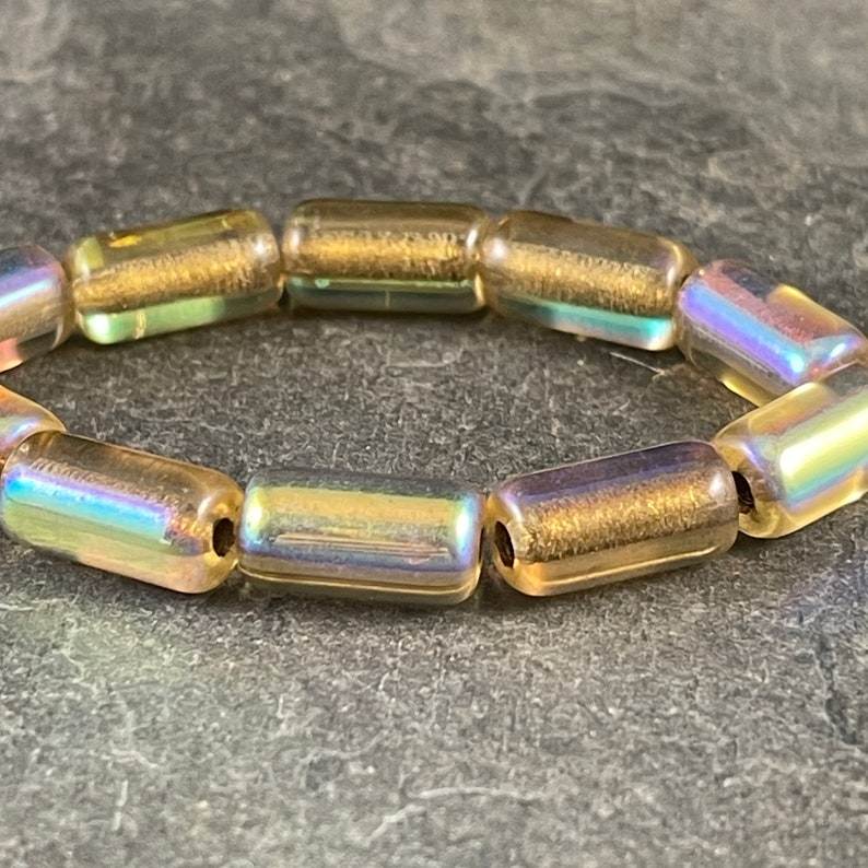 May include: A gold iridescent bracelet made of cylindrical beads.