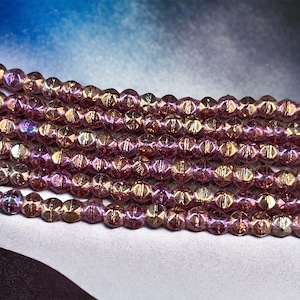 May include: Close-up of several strands of faceted beads. The beads are a mix of purple and gold, with a shimmering, iridescent quality. The beads are strung together, creating a delicate and elegant appearance. Ideal for jewelry making.
