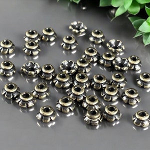 May include: A group of antique gold-toned metal bead caps with a scalloped edge. The bead caps are scattered on a gray surface.