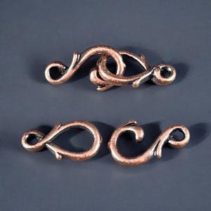 May include: Two antique copper-toned metal clasps with a decorative floral design. The clasps are designed to be used as a closure for necklaces, bracelets, or other jewellery.