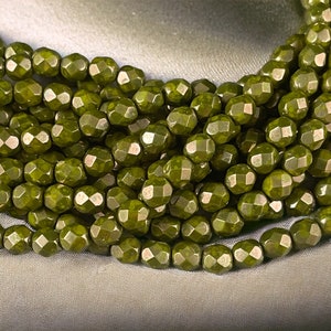 May include: A strand of dark green faceted glass beads. The beads have a slightly irregular, textured surface.