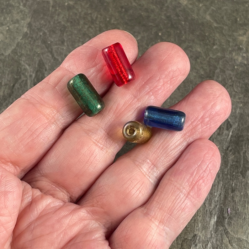 May include: Four glass beads in different colors: red, green, blue, and gold. The beads are cylindrical and have a smooth, shiny finish.