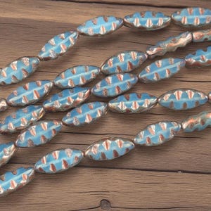 May include: Strands of oval-shaped beads with a light blue center and silver-colored edges. The beads have a pattern of reddish-brown shapes. The beads are strung together, creating a decorative element.