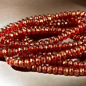 May include: A strand of red faceted glass beads. The beads are small and have a metallic sheen.