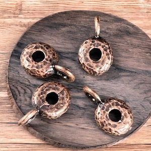 May include: Four antique gold-toned metal rings with a hammered texture and a circular hole in the center. Each ring has a small loop at the top for hanging.