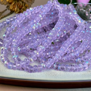May include: A strand of iridescent lavender glass beads. The beads are faceted and have a slightly irregular shape.