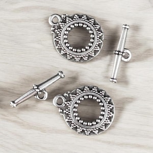 May include: Two silver-toned toggle clasps with ornate circular designs and a silver-toned barrel clasp.