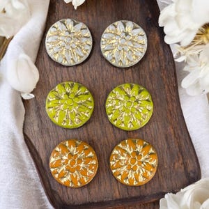 May include: Six round ceramic buttons with a gold floral design. The buttons are in three colors: white, yellow-green, and orange.