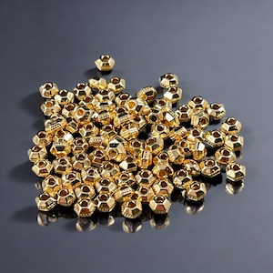 May include: A large pile of gold-colored metal beads. The beads are faceted and have a small hole in the center. The beads are arranged in a random pattern.