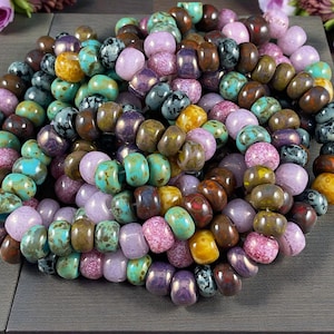 May include: A collection of colorful, irregular beads in shades of turquoise, purple, brown, yellow, and pink. The beads are strung together, creating a textured and vibrant display. The beads appear to be made of glass or a similar material.