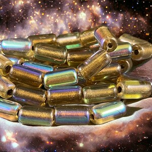 May include: A pile of iridescent gold glass beads with a metallic sheen. The beads are cylindrical and have a hole in the center for stringing.