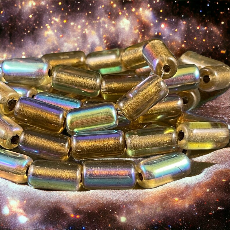 May include: A pile of iridescent gold glass beads with a metallic sheen. The beads are cylindrical and have a hole in the center for stringing.