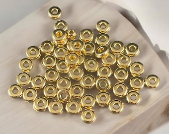 May include: A collection of small, round, gold-colored metal spacer beads. Each bead features a smooth, reflective surface with a central circular hole, designed for jewelry making and stringing projects. The beads are uniform in shape.