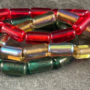 May include: A close-up of a strand of glass beads in red, green, and iridescent gold. The beads are cylindrical and have a slightly textured surface.