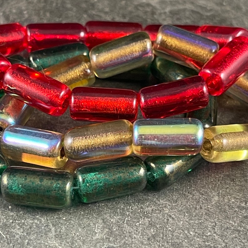May include: A close-up of a strand of glass beads in red, green, and iridescent gold. The beads are cylindrical and have a slightly textured surface.