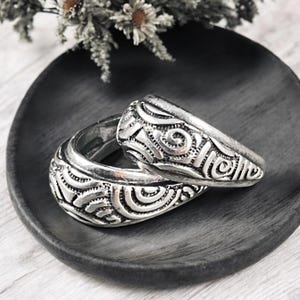 May include: Two silver rings with intricate swirling patterns. The rings are stacked on top of each other and are on a dark gray surface.